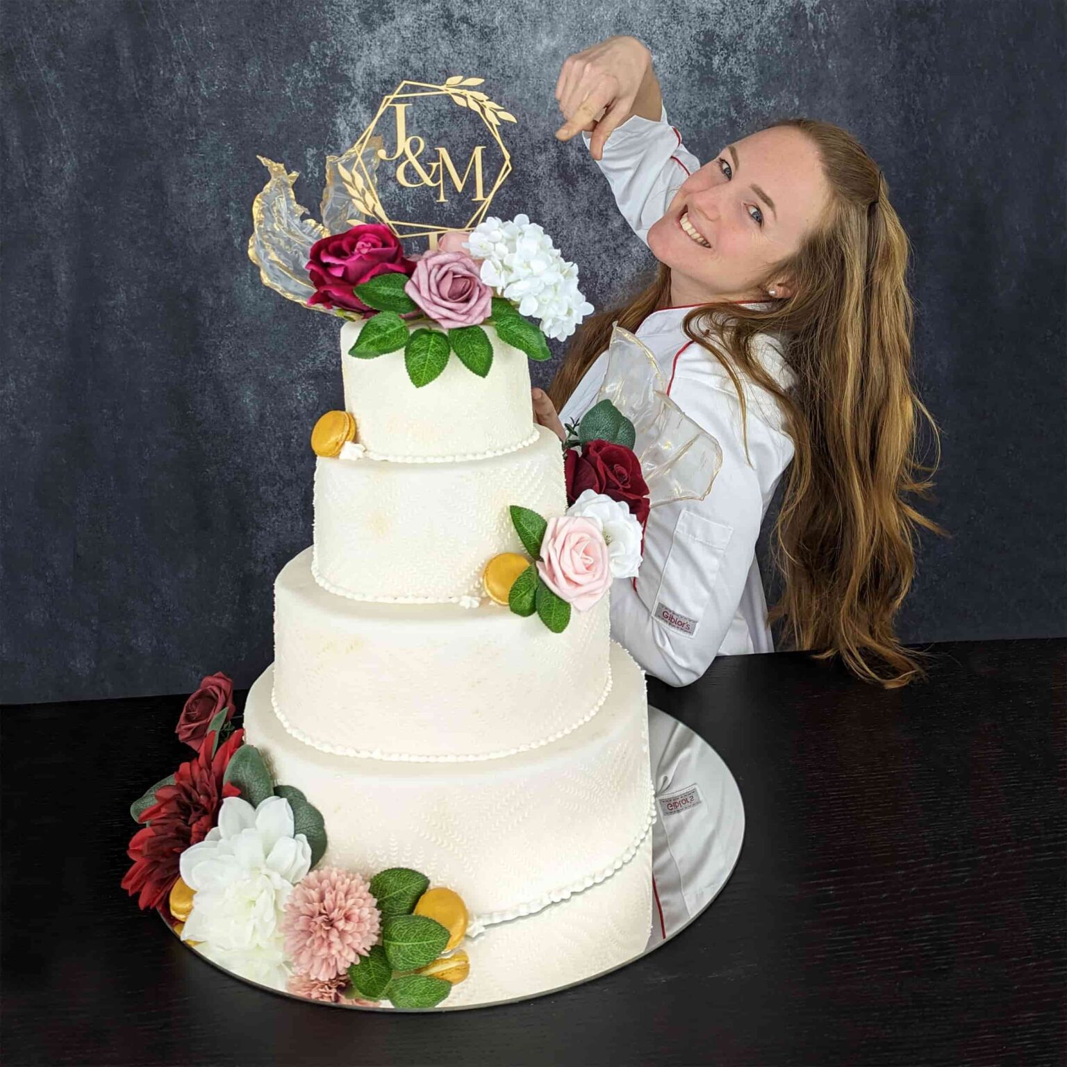 Julia Baumgartner hinter einer Hochzeitstorte in weiß mit 4 Elementen und blumen