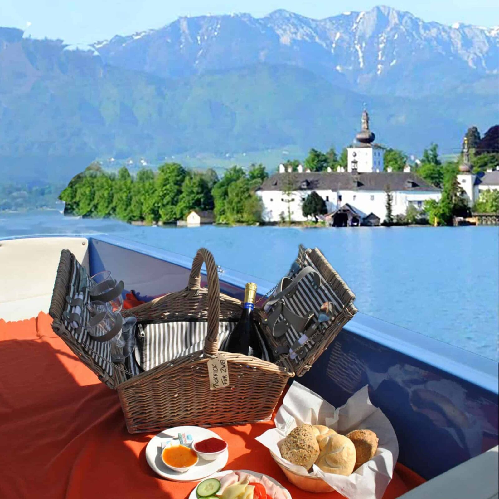 Boot am Traunsee mit Blick in die Berge und auf Schloss Ort. Im Boot ein Frühstück mit Brötchen, Marmelade und Getränken